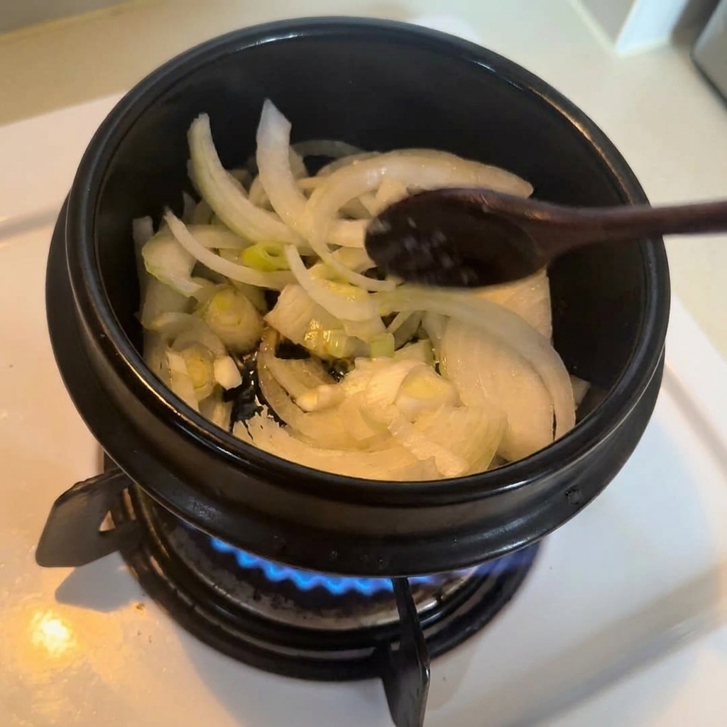コンロの上で、木製のスプーンを使って鍋の中の野菜を炒めている様子。