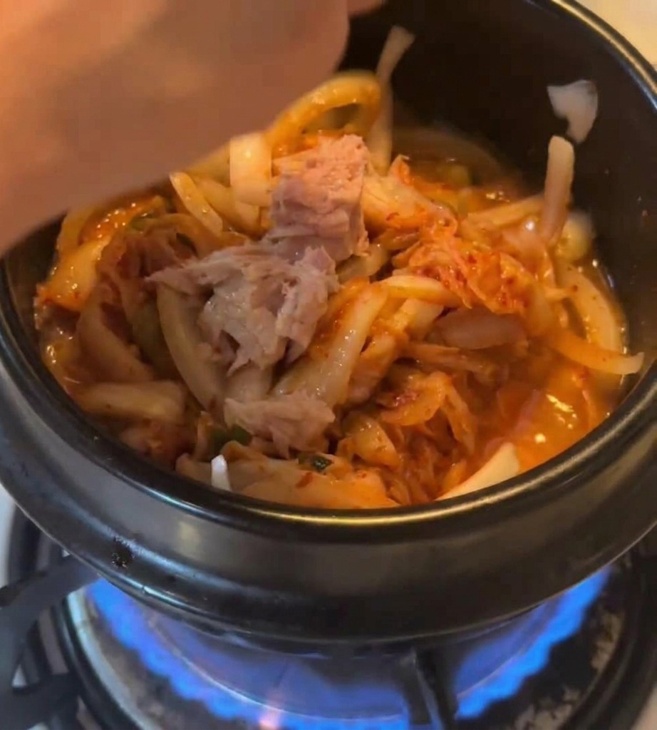 キムチと玉ねぎが入った鍋にツナの身を加えている様子。
