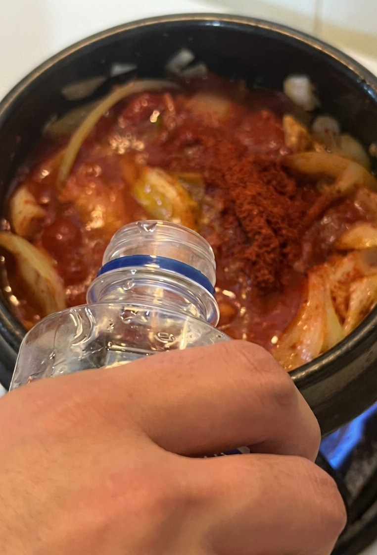 鍋に透明なボトルから水を注いでいる様子。