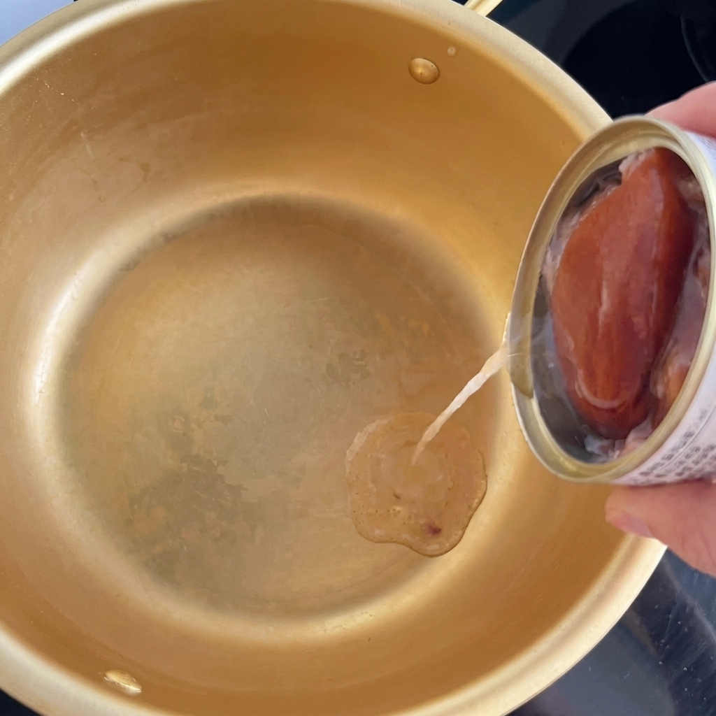 金色の小鍋にツナ缶からオイルだけを注いでいる様子。