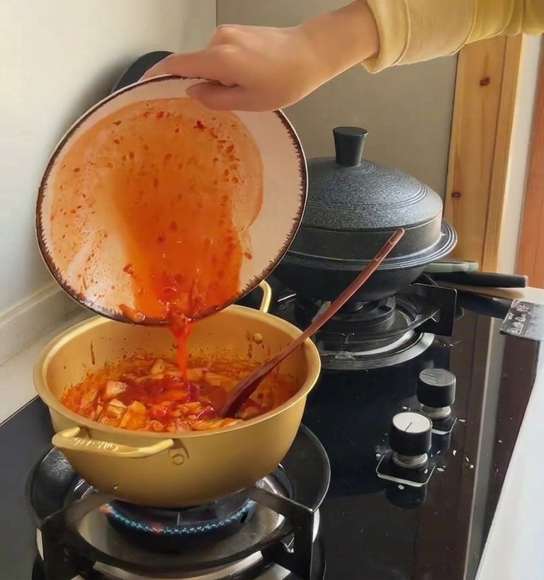 真っ赤なキムチの汁を鍋に注ぎ入れている様子。