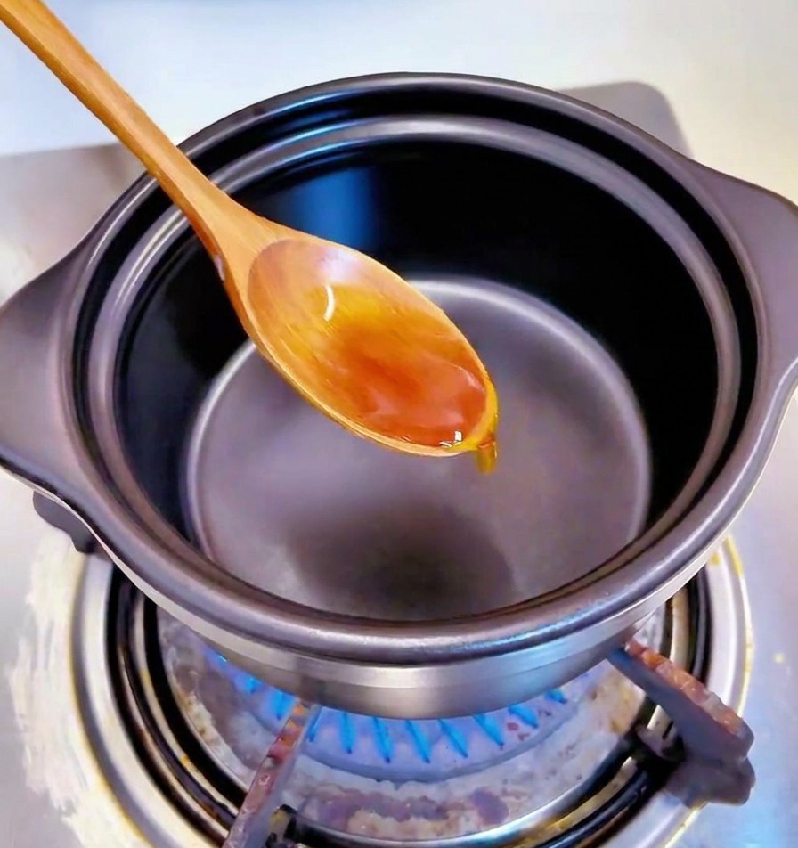 黒い鍋の底で、油と一緒にみじん切りのにんにくを木のスプーンで炒めている様子。