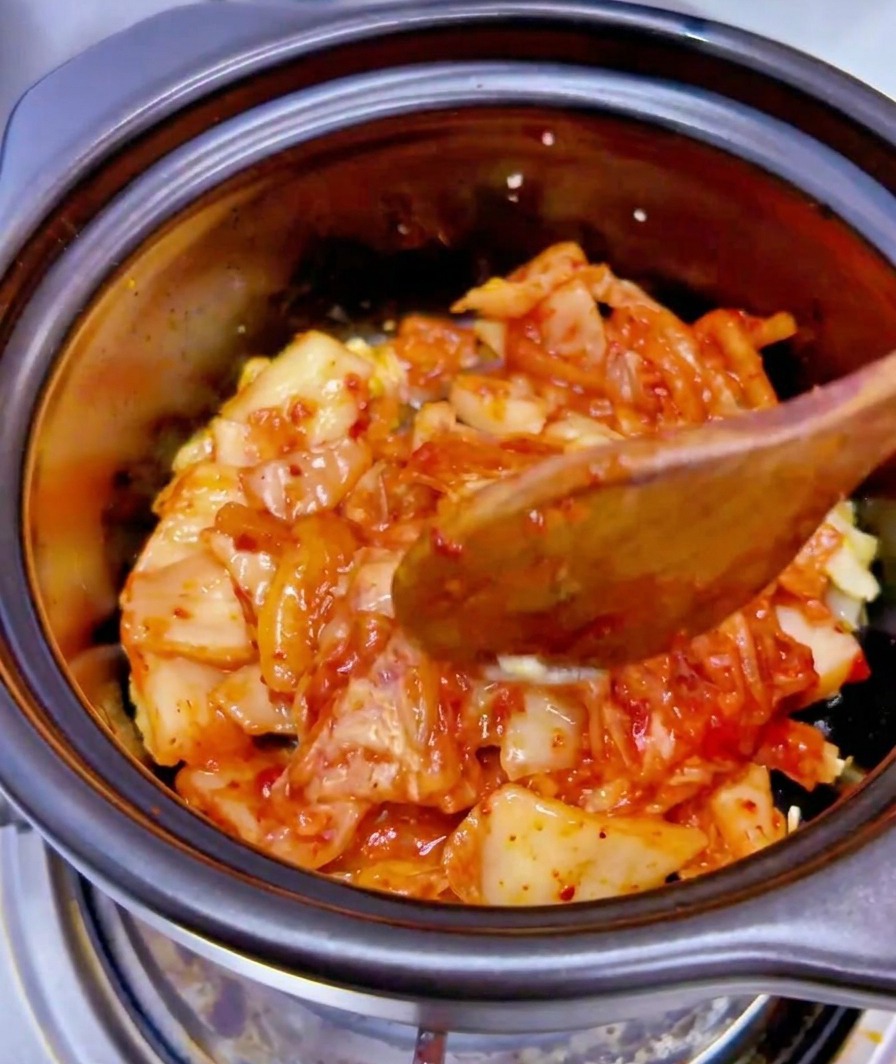 刻んだキムチとにんにくが入った黒い鍋に、ツナ缶の汁を注いでいる様子。