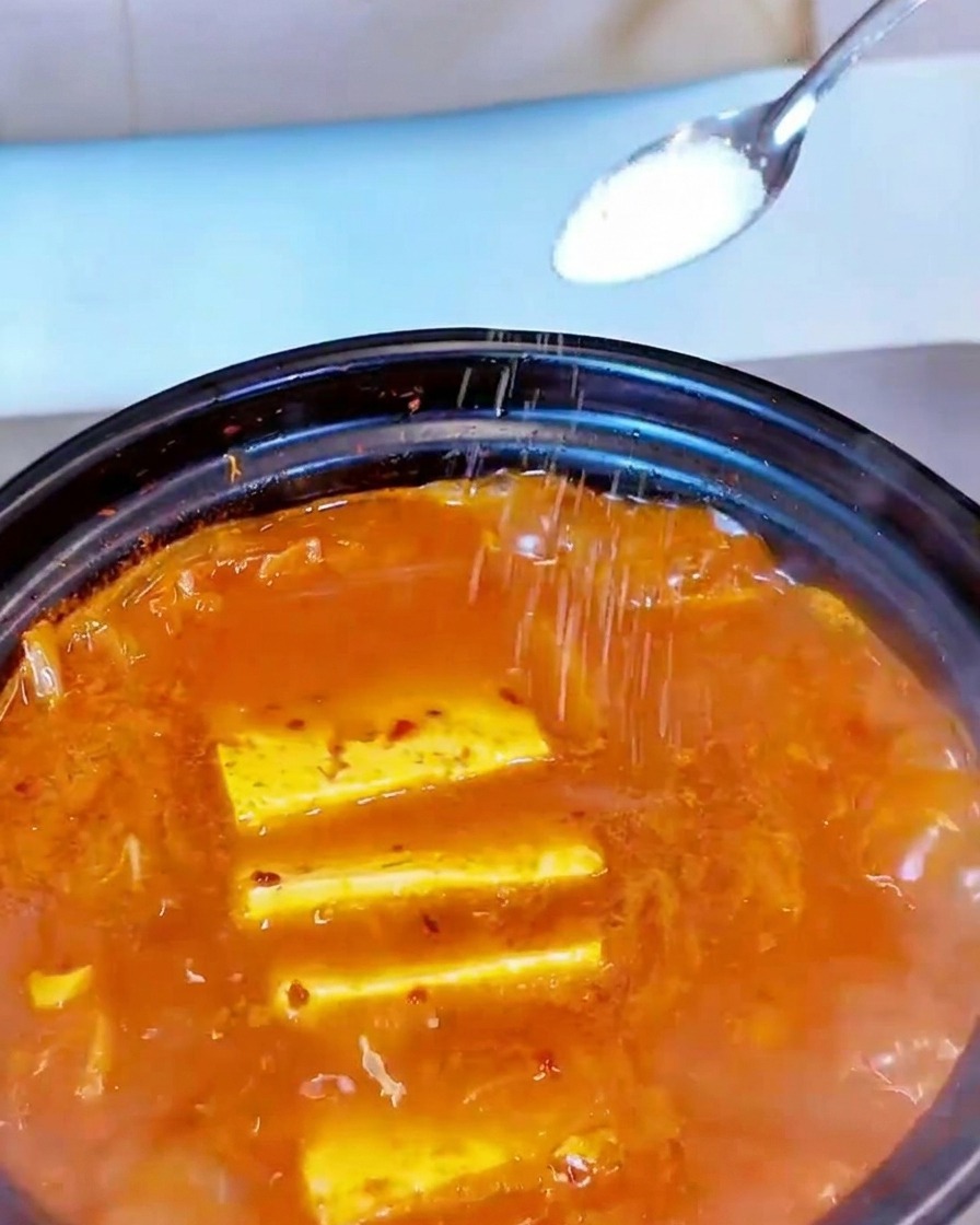 煮立っている赤いスープの表面に、小さなスプーンから白い塩を振りかけている様子。