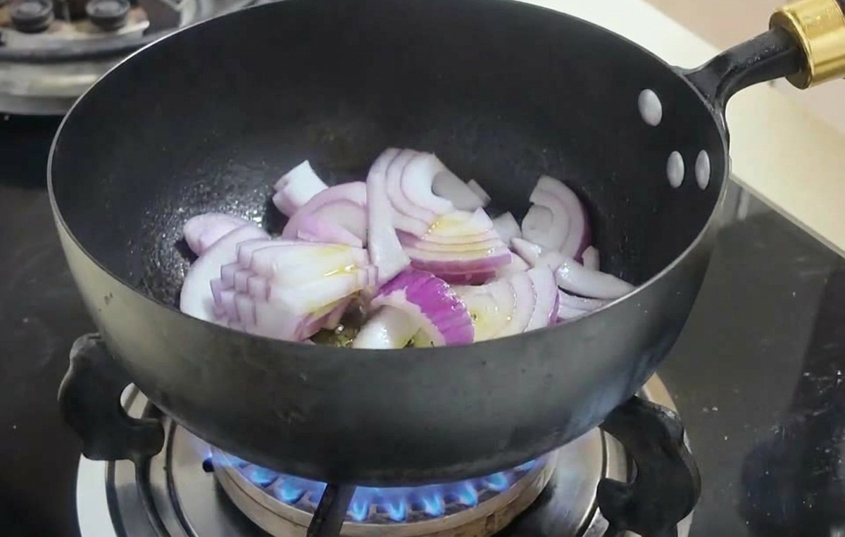 黒い鍋の中で赤玉ねぎがしんなりするまで炒められている様子。