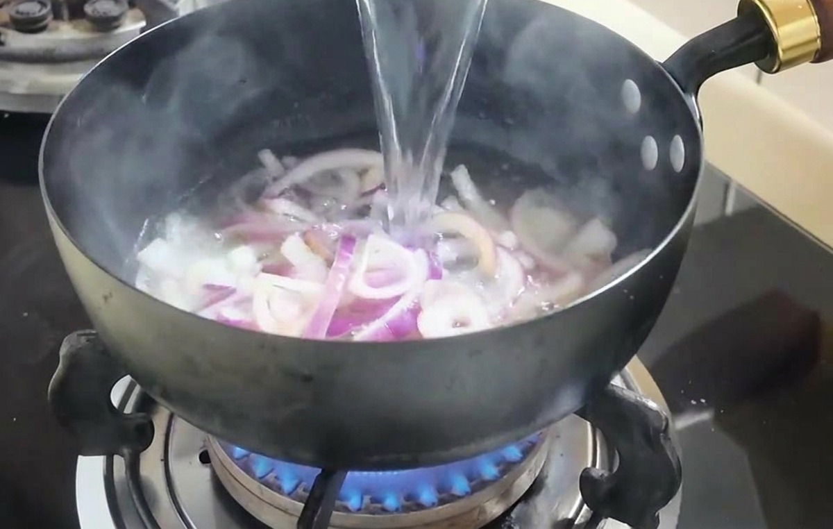 炒めた玉ねぎが入った鍋に、ボウルから水を注ぎ入れている様子。