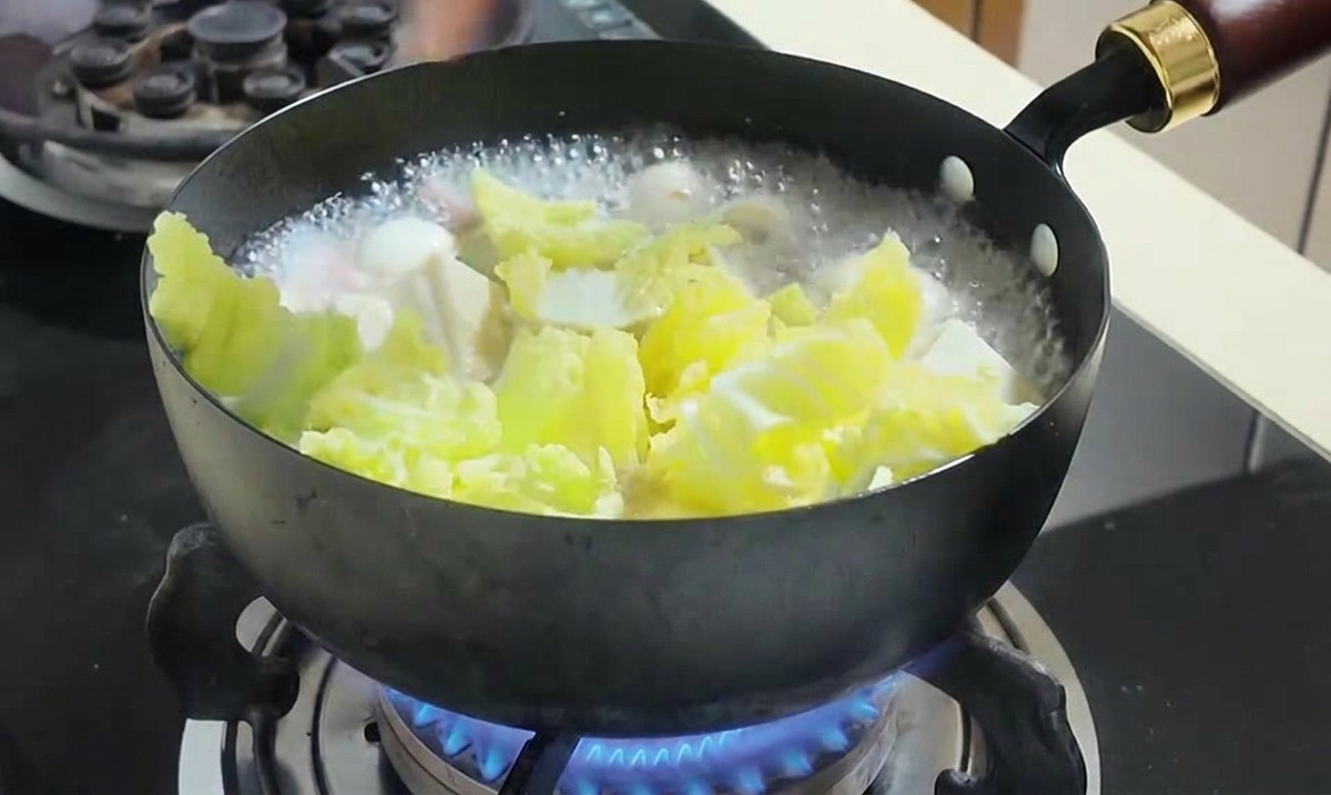 煮え立った鍋に黄色いコーンと刻んだ白菜を追加している様子。