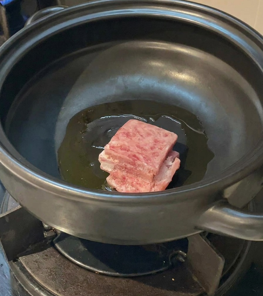 熱した土鍋に、脂ののった豚バラ肉のスライスを入れている様子。