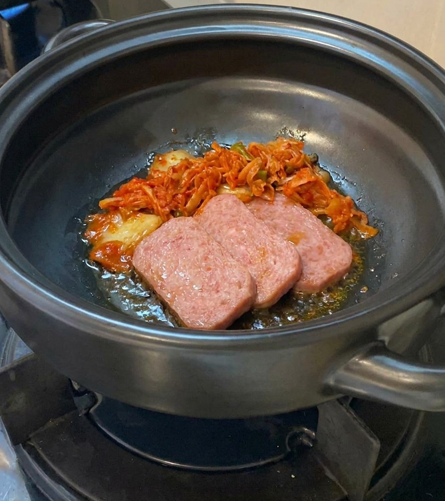 肉を炒めている土鍋に、刻んだキムチを投入している様子。