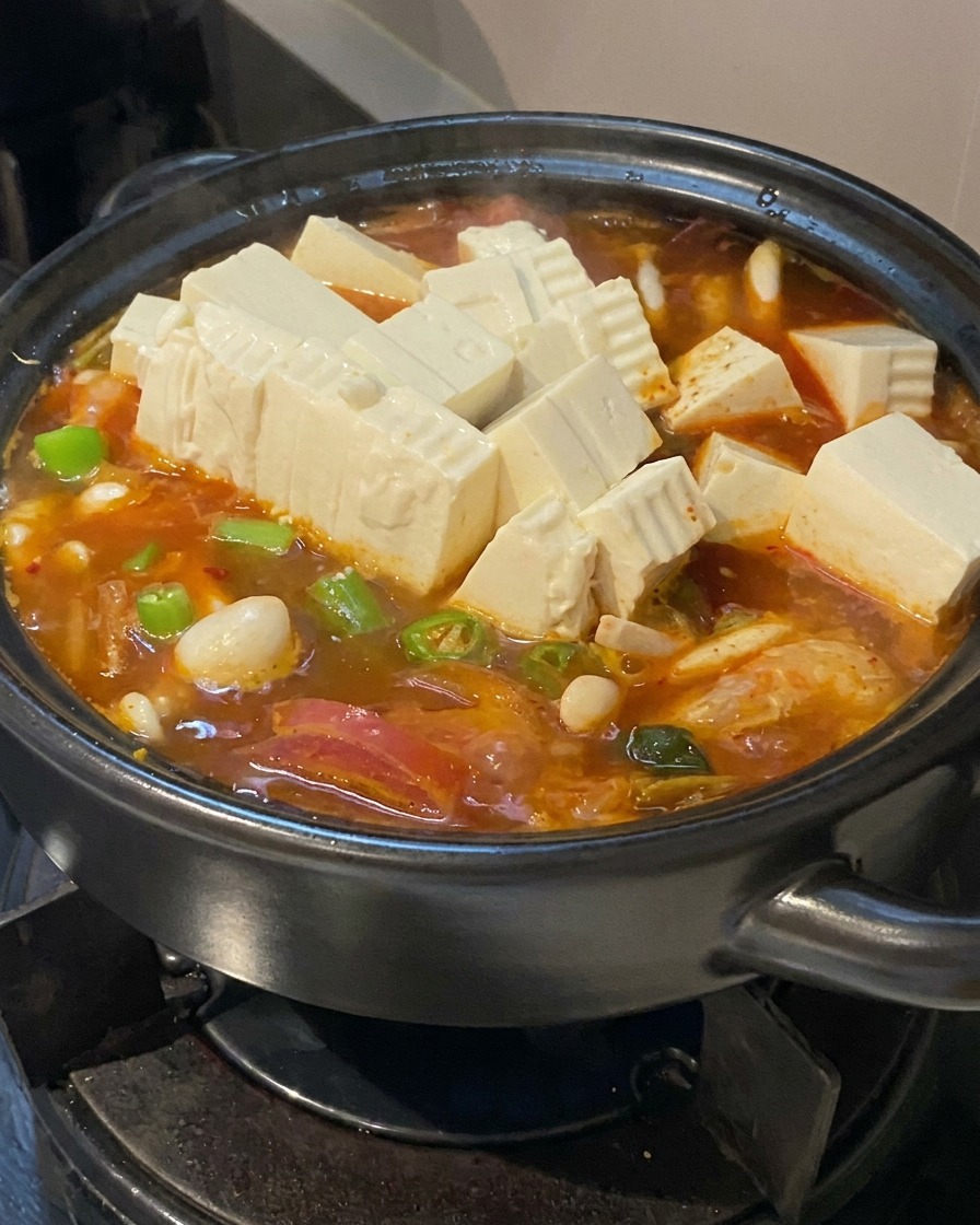 煮え立つ鍋に、角切りの豆腐とスライスした青唐辛子を投入している様子。