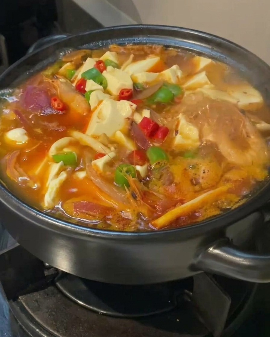 完成間近のキムチチゲ。豆腐の上に赤と緑の唐辛子が美しく飾られている接写写真。