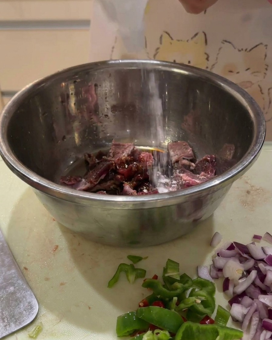 ボウルに入った牛肉の角切りに、ボトルから色の濃い調味料を注いでいる様子。