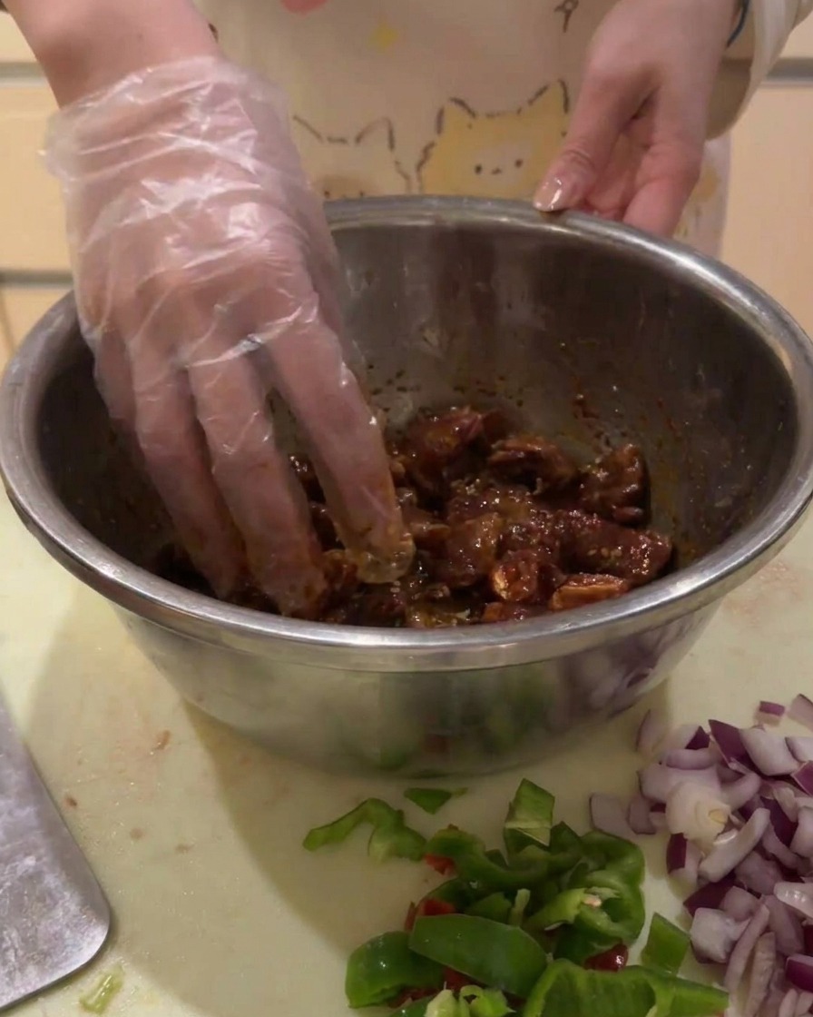 手袋をした手で、ボウルの中の牛肉と調味料をしっかり混ぜ合わせている様子。