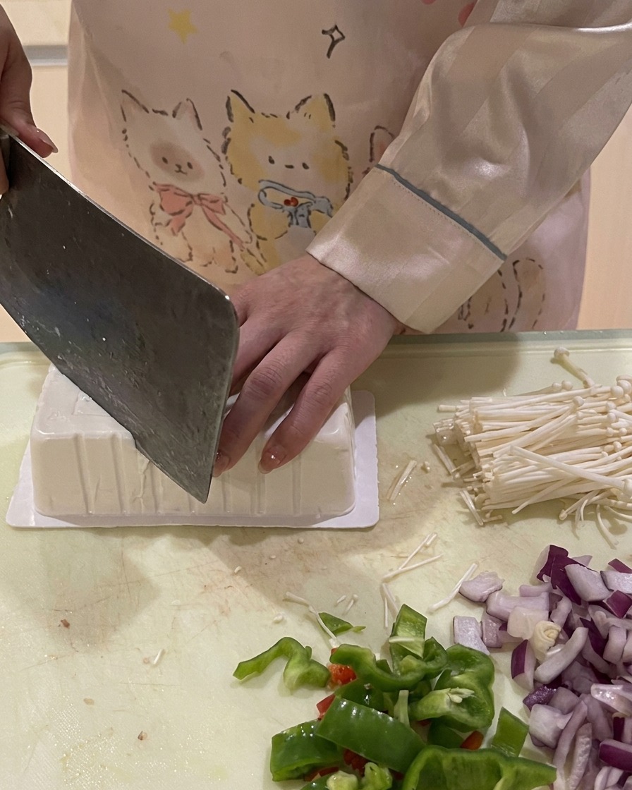 逆さまにした豆腐パックの角を包丁で切り、空気を入れて取り出しやすくしている様子。