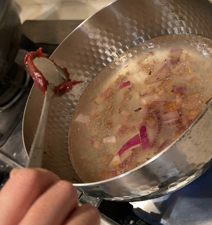 水が入った鍋に、スプーン一杯の濃厚な赤いコチュジャンを溶かし入れている様子。