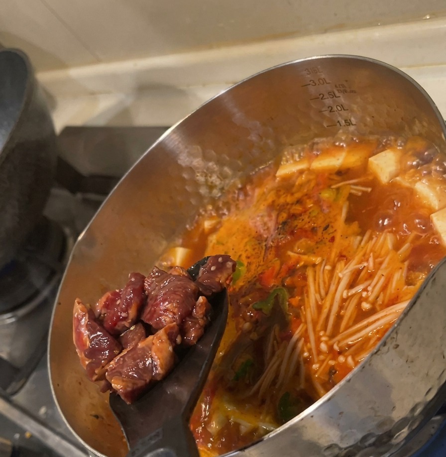 沸騰したスープの中に、味付けした生の牛肉をヘラで滑り込ませている様子。