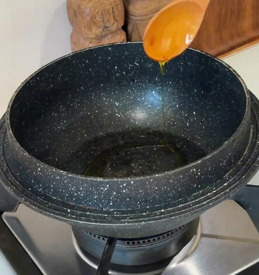 石鍋に木のスプーンで食用油を引いている様子。