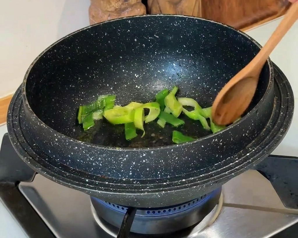 石鍋の中で長ねぎを木のスプーンで炒めている様子。