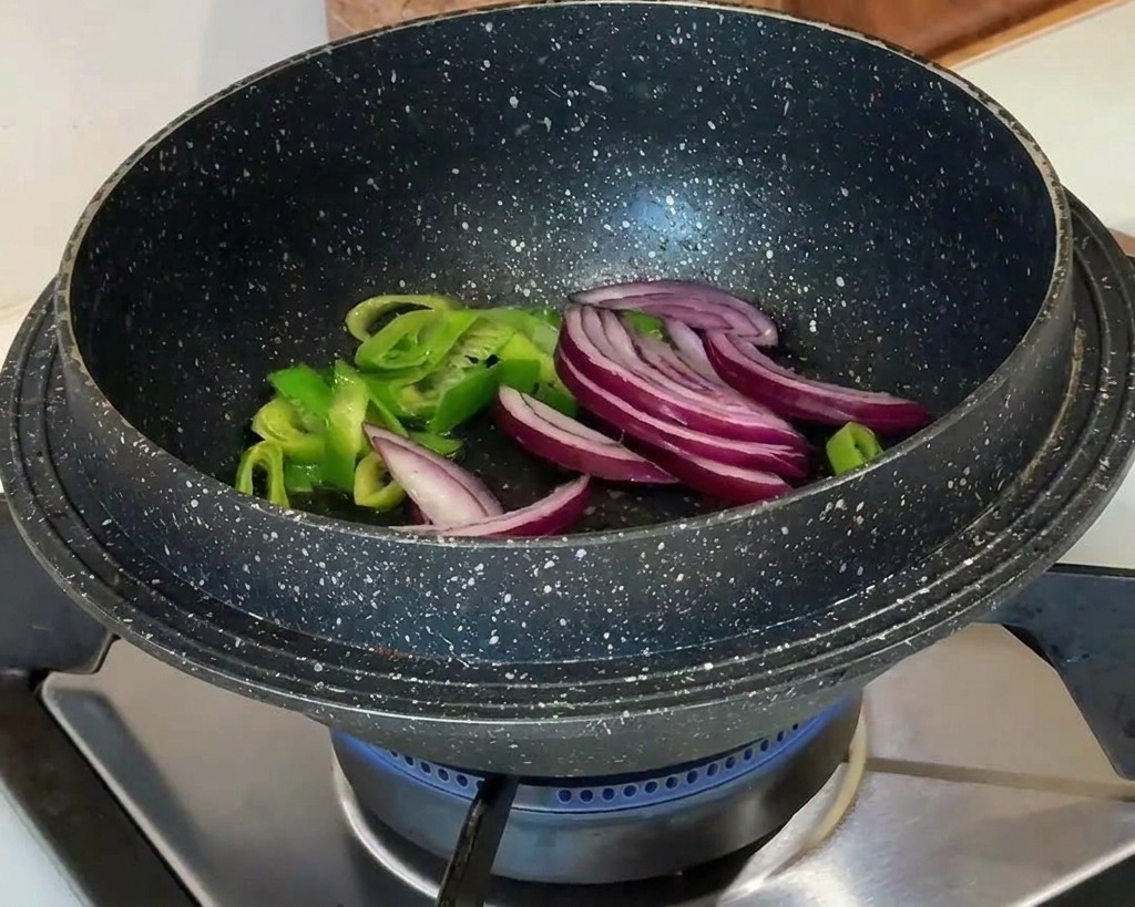 炒めた長ねぎの中に赤玉ねぎのスライスを加えている様子。