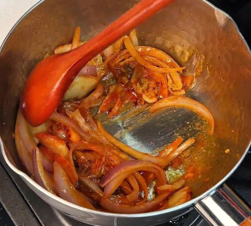 鍋の中でキムチと玉ねぎを木べらで混ぜ合わせる様子