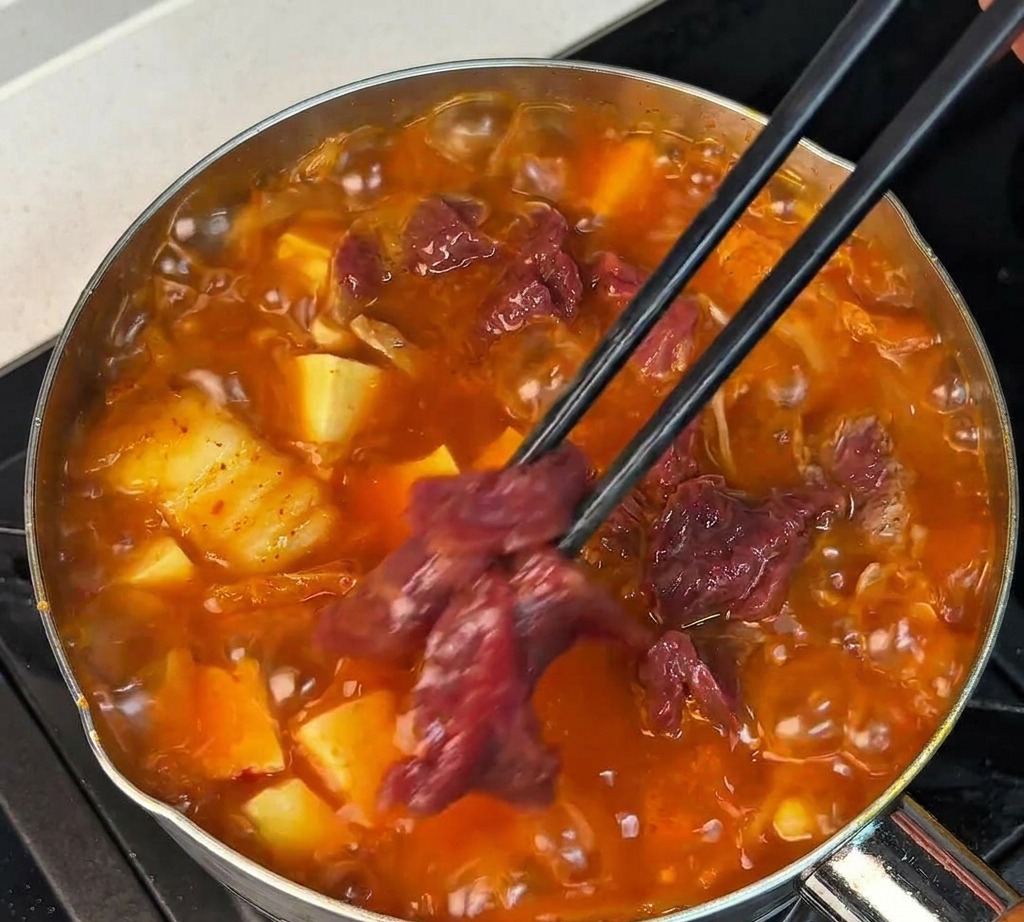 黒い箸で牛肉をスープに広げながら入れる様子
