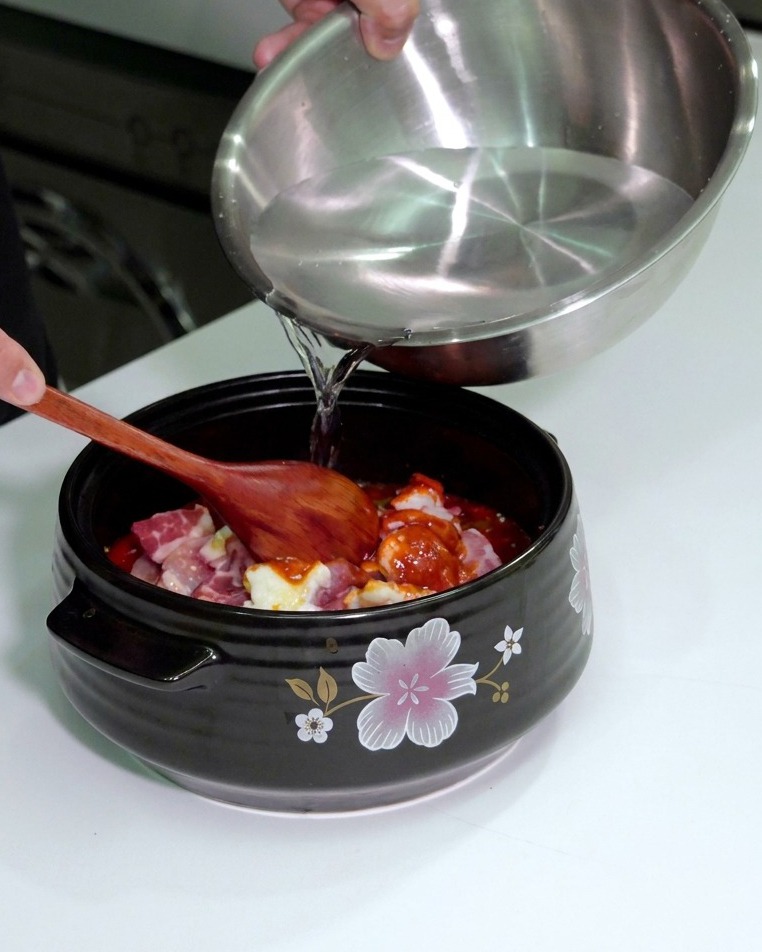 調味料を乗せた具材が浸るまで、鍋に水を注ぎ入れている様子