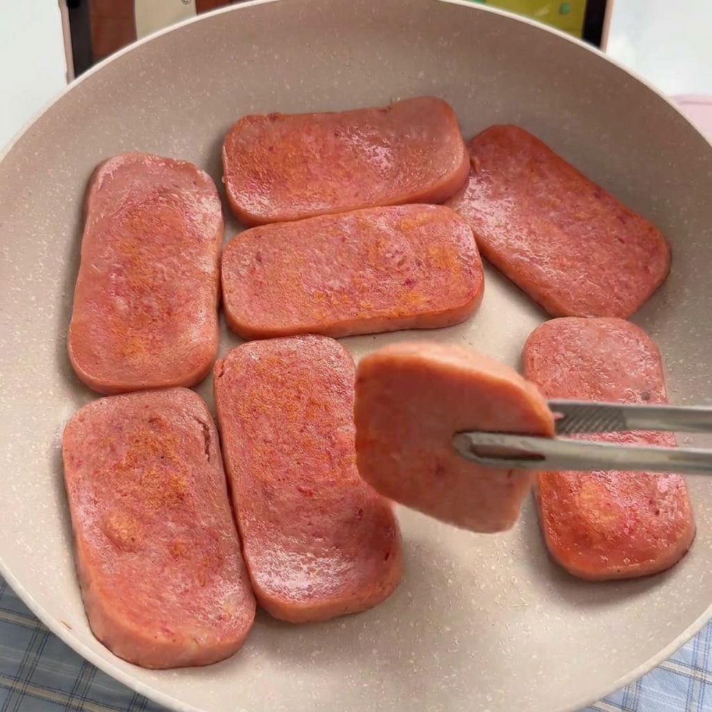 薄ピンク色のランチョンミートをフライパンでこんがりと焼く様子