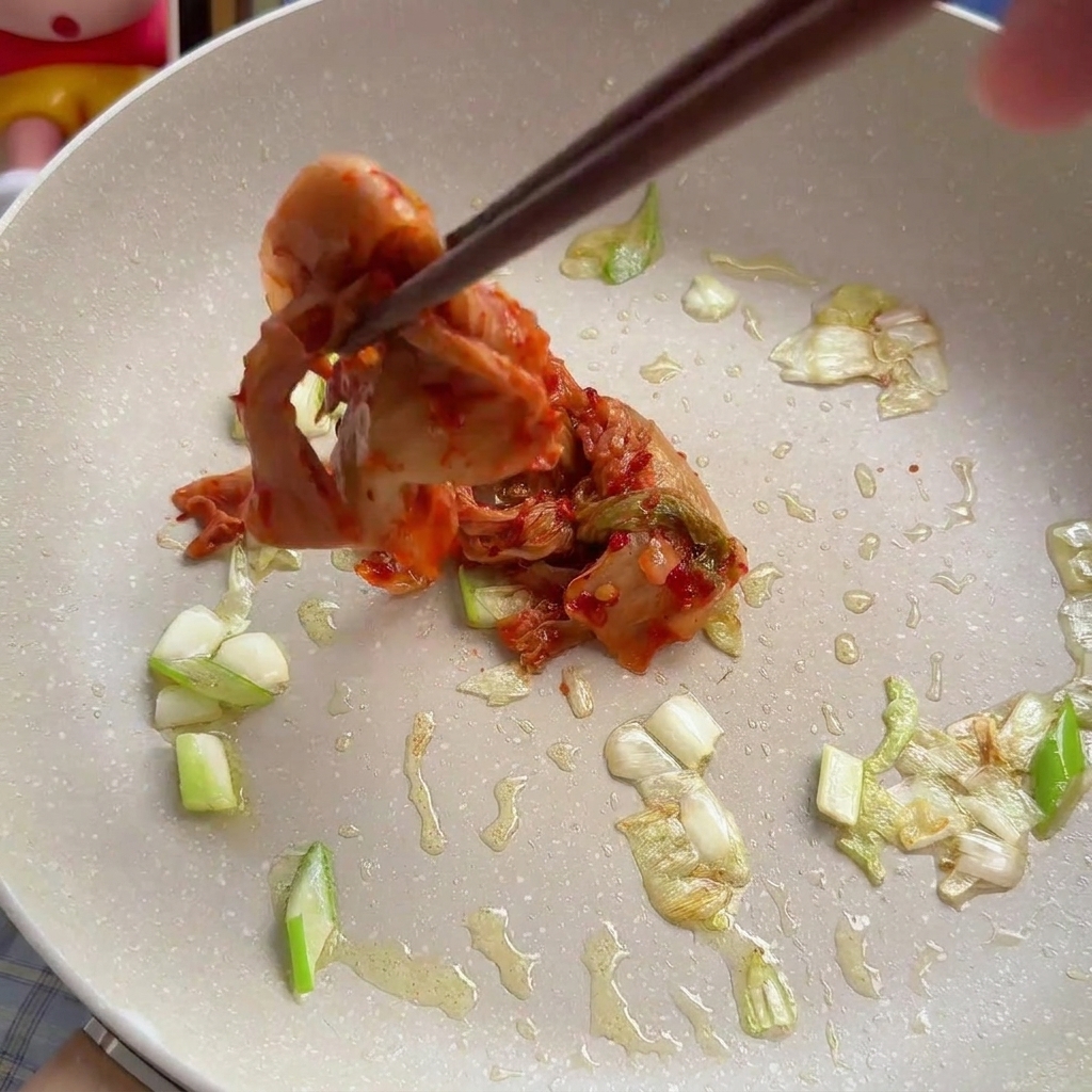 炒めたねぎの中に白菜キムチを加える様子