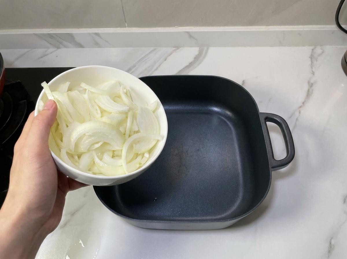 黒い鍋の底に、スライスした玉ねぎを丁寧に敷き詰めている様子。