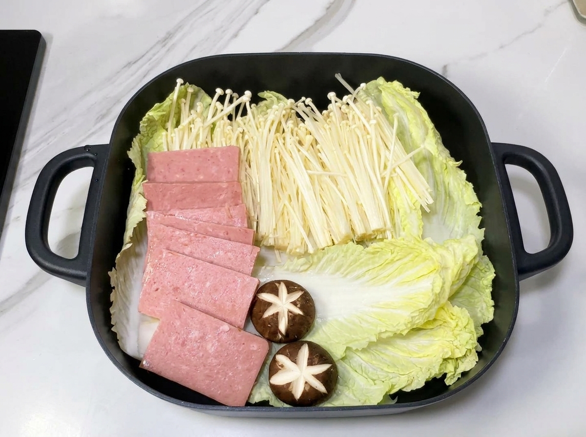 玉ねぎを敷いた鍋の上に、白菜、えのき、スパムが美しく配置された様子。