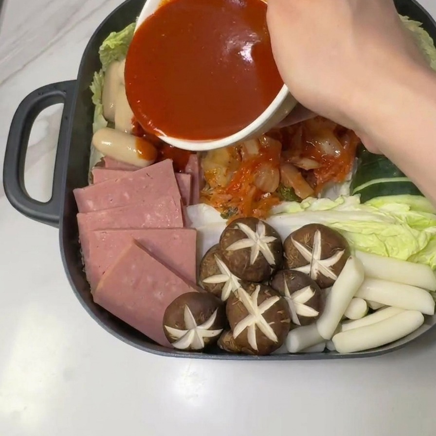 盛り付けた具材の中央に、赤いコチュジャンタレをかけている様子。