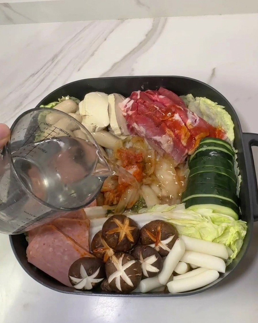 具材が綺麗に並んだ鍋に、計量カップから水を注いでいる様子。