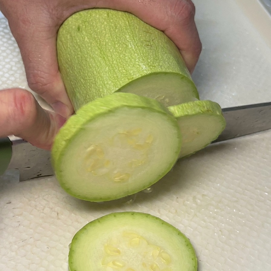 まな板の上でズッキーニを輪切りにしている様子