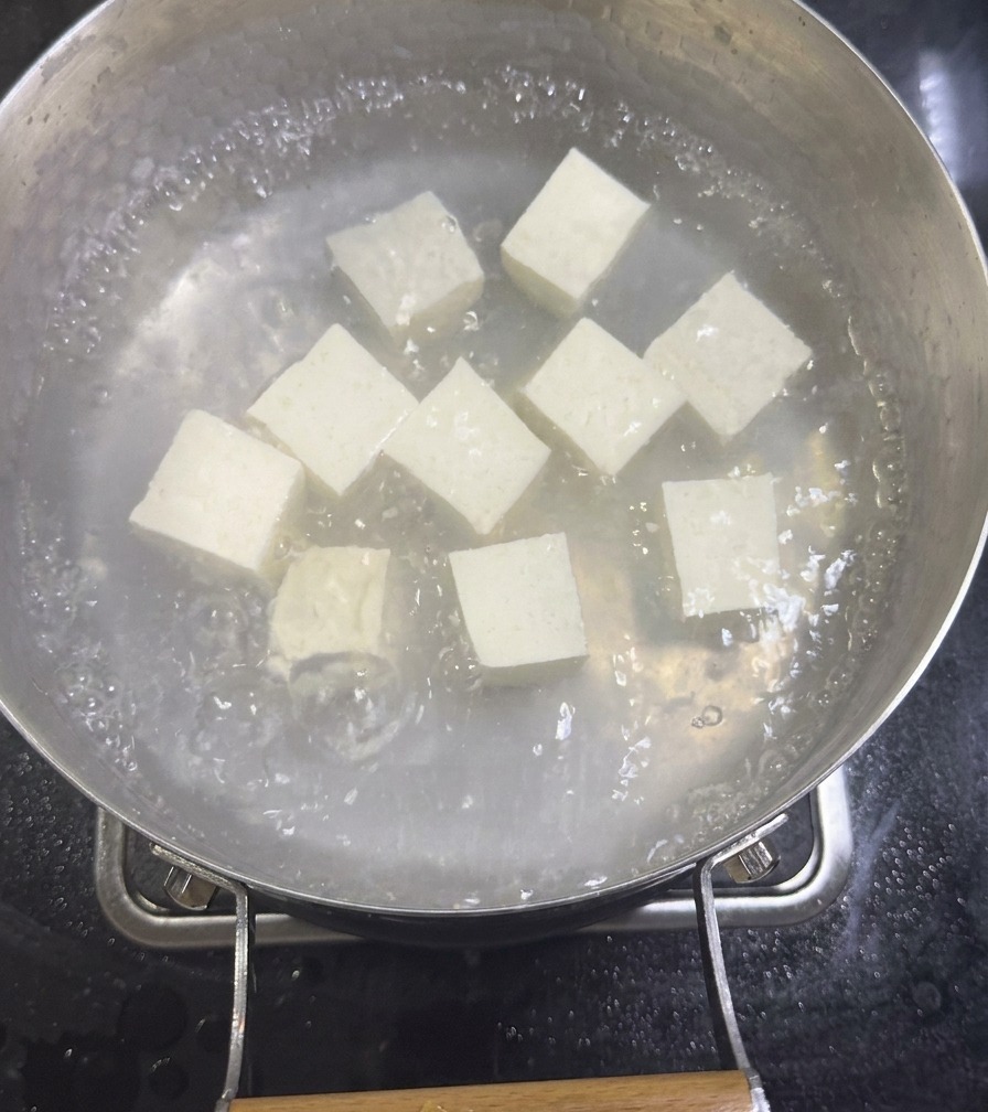 沸騰したハマグリの出汁の中で、白くて柔らかそうな絹ごし豆腐の角切りが煮えている様子。