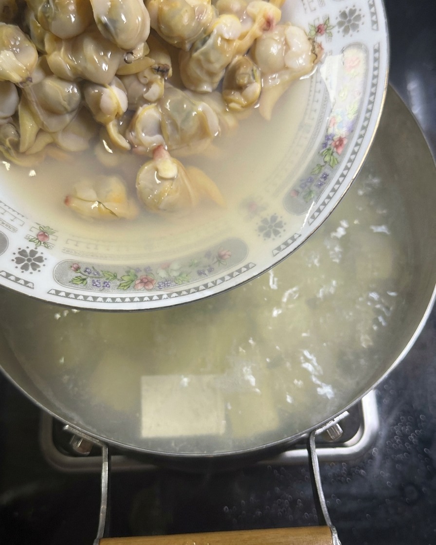 豆腐のスープに、殻から外したハマグリの身を戻し入れている様子。