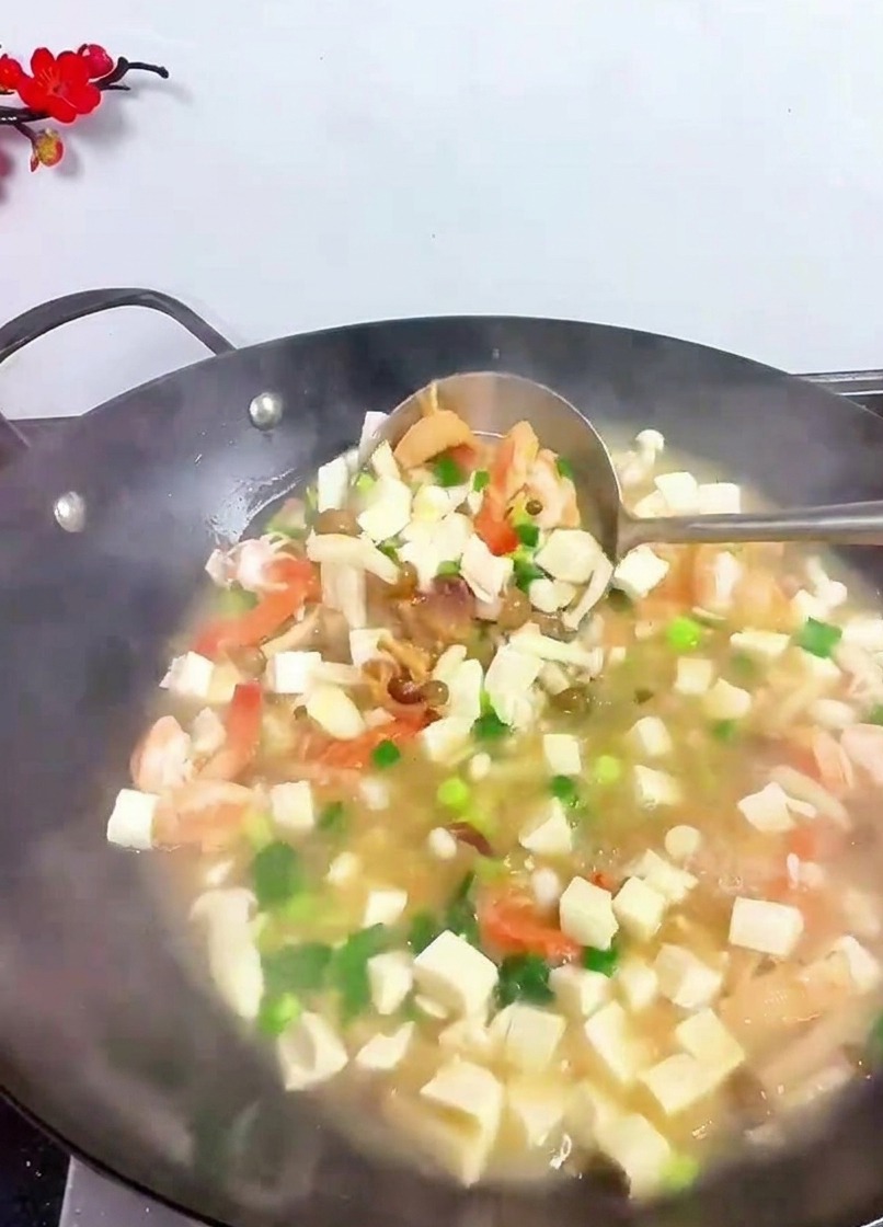 お玉で豆腐やエビ、野菜を優しく混ぜ合わせている様子。