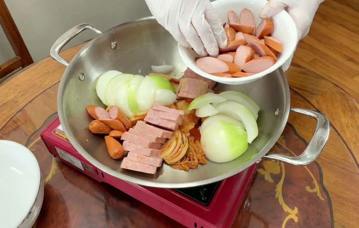 玉ねぎやスパムが入った鍋に、スライスされたソーセージを敷き詰めている様子。