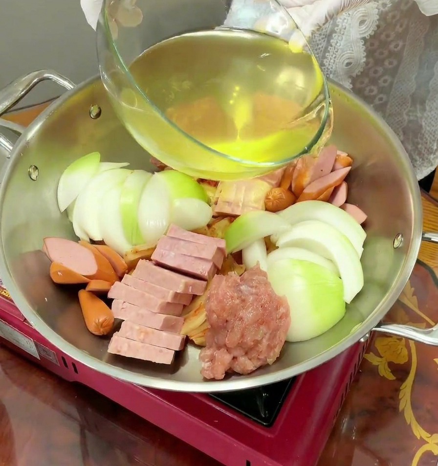 具材が並べられた鍋に、透き通った黄金色の出汁をゆっくりと注ぎ入れている様子。
