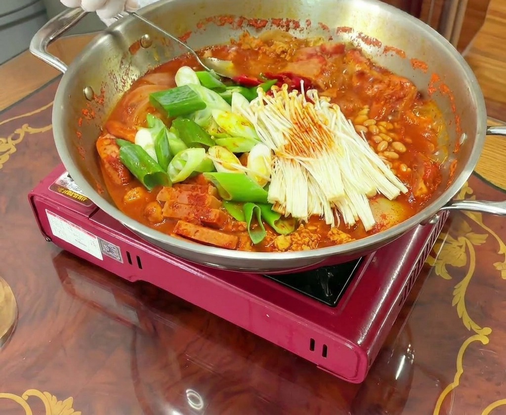 グツグツと煮える鍋をかき混ぜ、最後にラーメンの麺とスライスチーズをのせる様子。