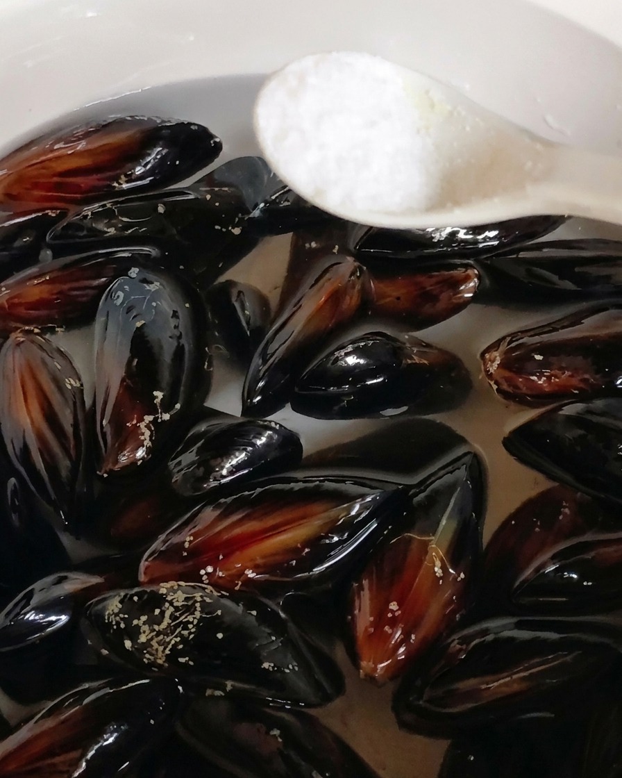 水に浸かったムール貝の入った鍋に、スプーン一杯の塩を加えている様子。