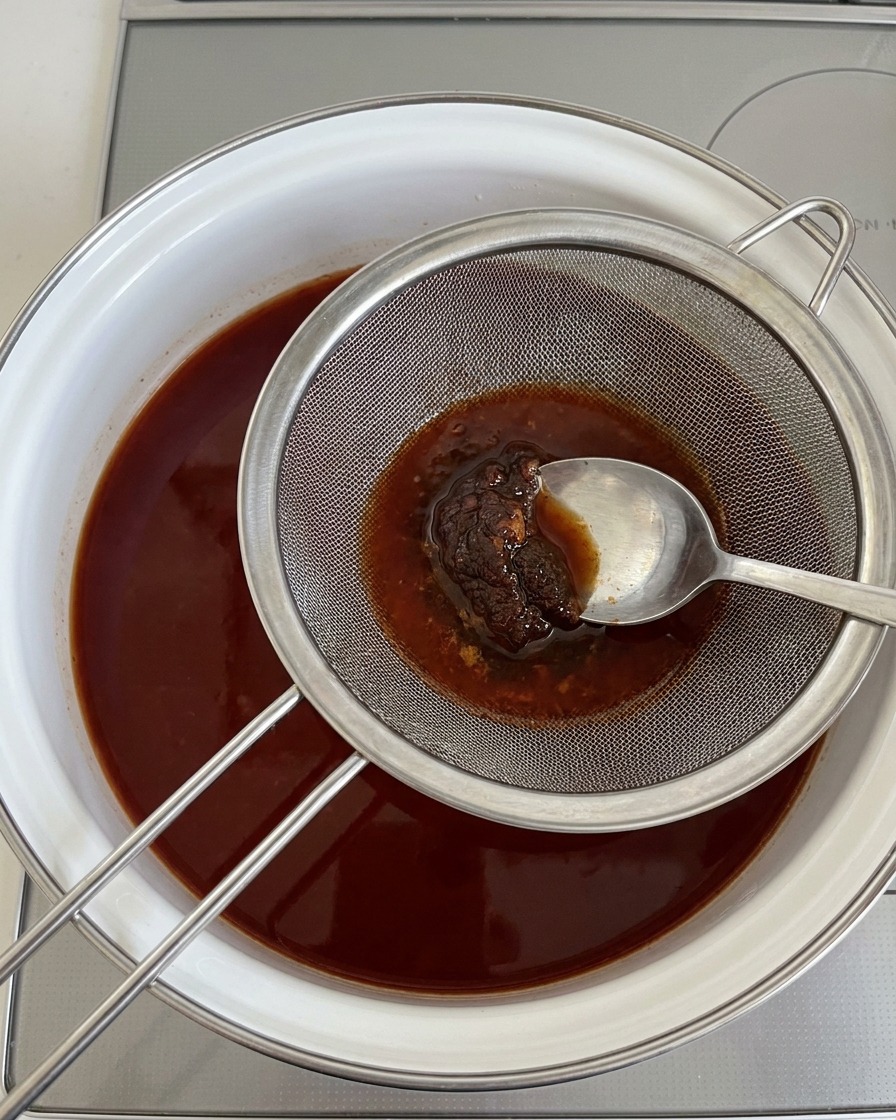 沸騰した出汁の上で、金属製の味噌こしにスプーンを押し当てて、とろみのある味噌を溶かしている様子。
