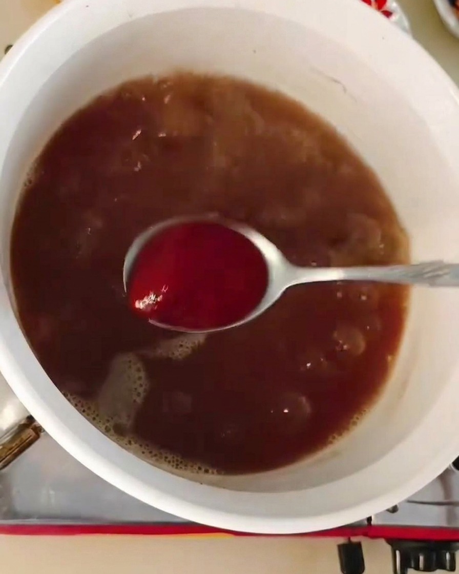 ふつふつと煮える濃い茶色のスープに、スプーン一杯の赤いコチュジャンを混ぜ合わせている様子。