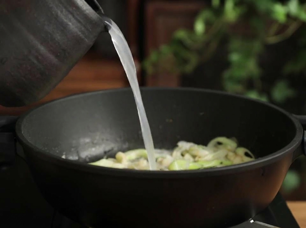 炒めた野菜の入った鍋に米のとぎ汁を注ぐ様子