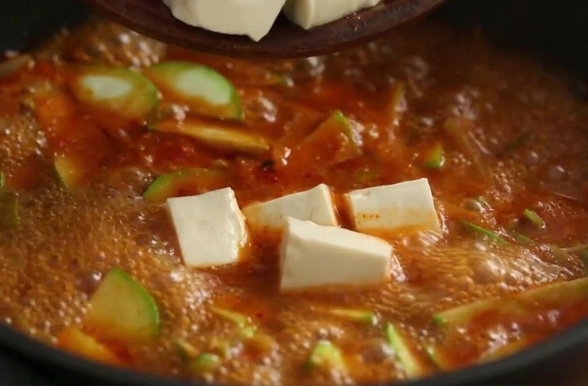 ぐつぐつ煮えるチゲに豆腐を入れる様子