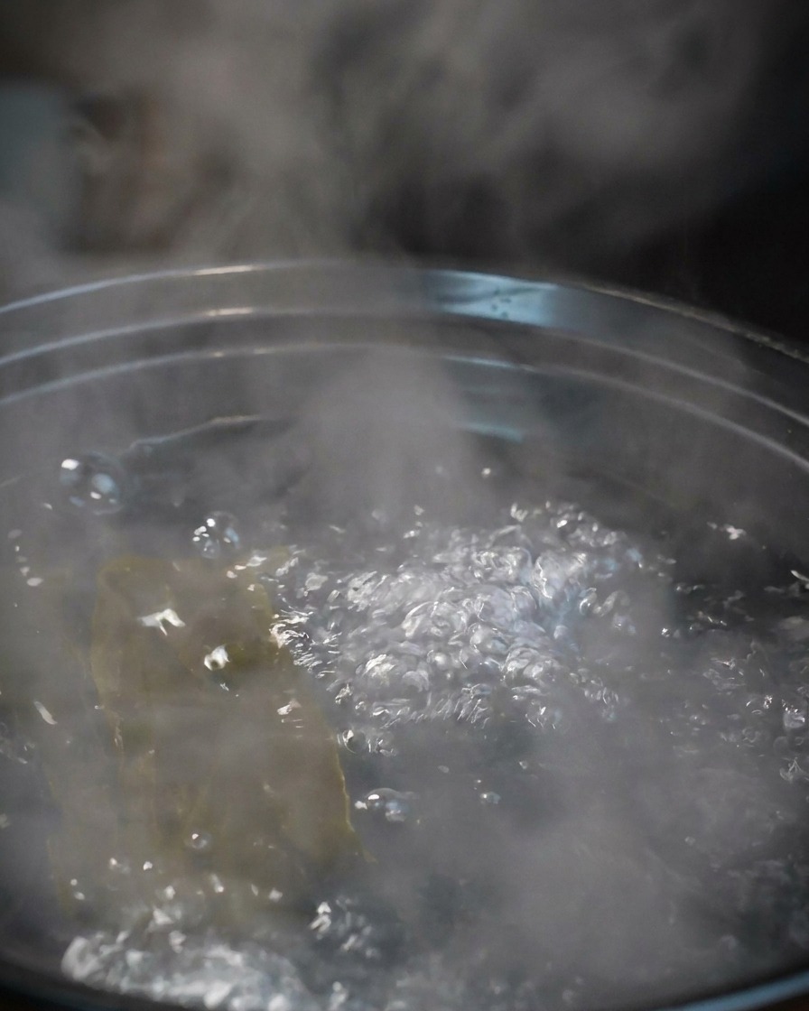 昆布だしの入った沸騰した鍋に、生の大エビを数匹入れている様子。