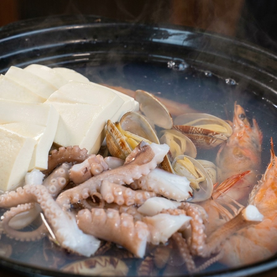 ヘラを使って、スライスした大根とにんじんを海鮮鍋に加えている様子。