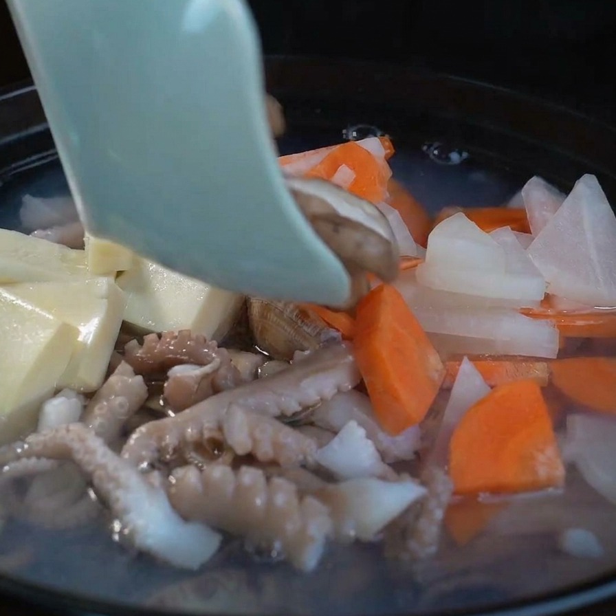 豆腐や野菜と一緒に、スライスした新鮮なしいたけを鍋に入れている様子。