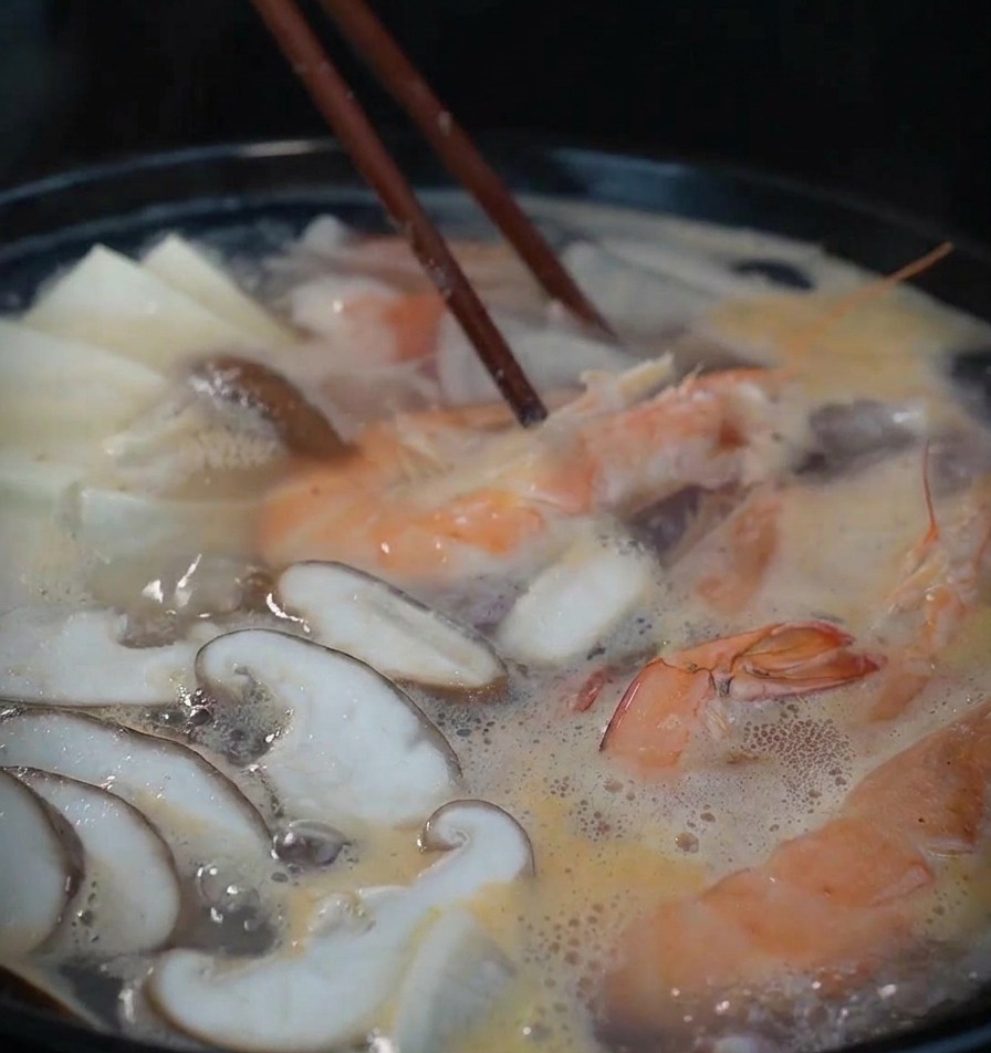 エビや豆腐が入った鍋を、木製の箸で優しく混ぜながら煮込んでいる様子。