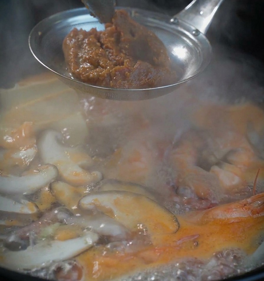 沸騰した鍋の上で、味噌こしに入れた濃厚な韓国味噌を準備している様子。