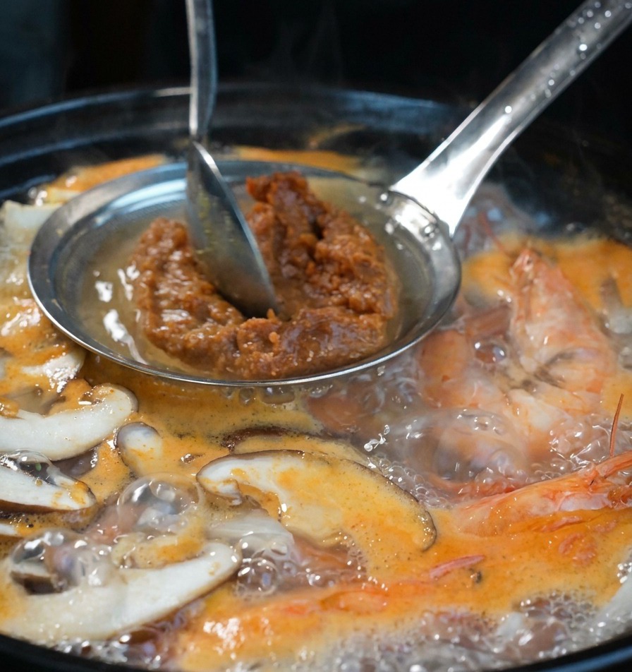スプーンを使って、味噌こしの中の韓国味噌をスープに溶かし入れている様子。